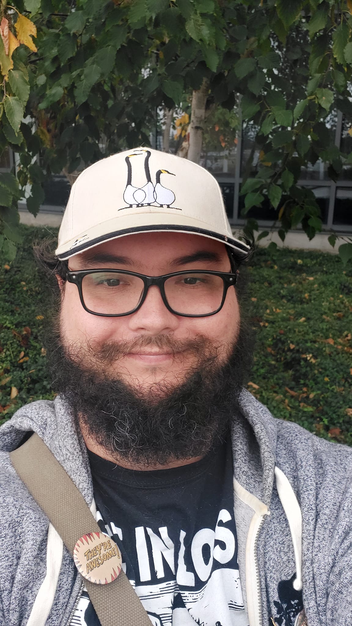 A man with short hair and bushy facial hair stands in a garden outside a hospital